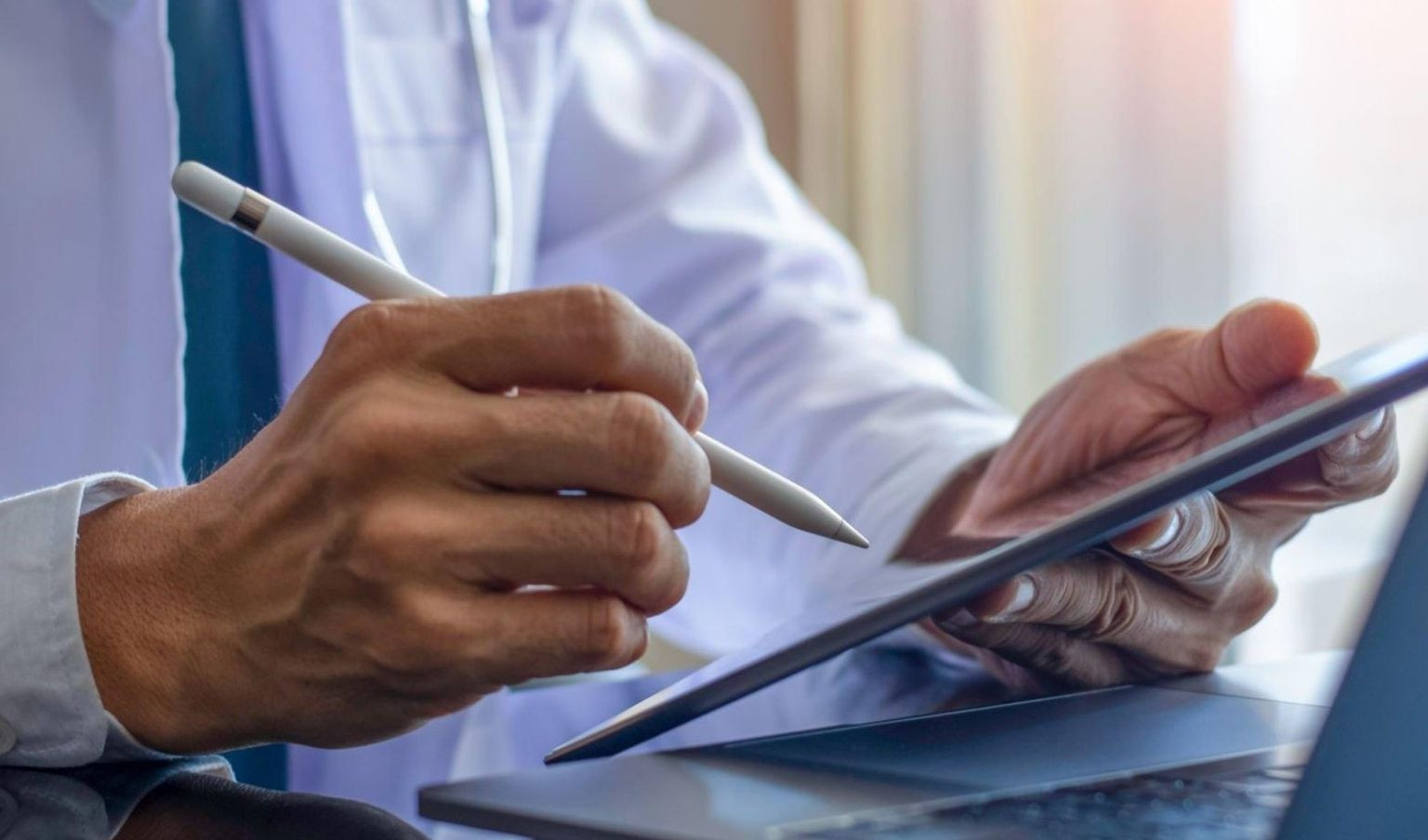 Medico con camice bianco e stetoscopio al collo utilizza un tablet con una penna digitale.